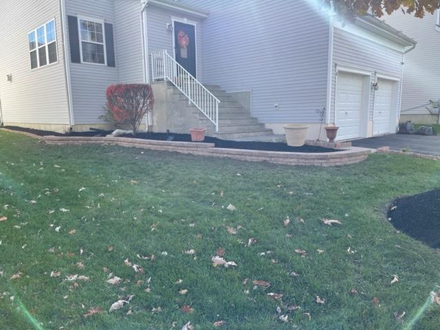 A house with a lawn, flower beds with dark mulch, and a set of stairs leading to the front door.