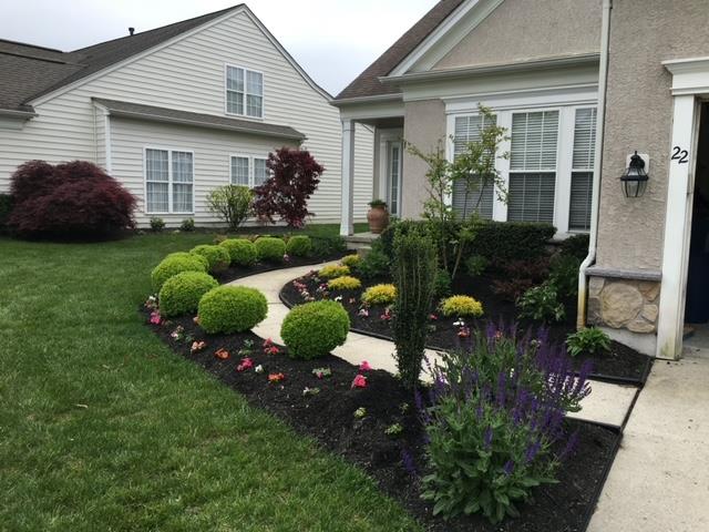 Curved walkway through a landscaped garden bed with rounded shrubs, colorful flowers, and dark mulch.