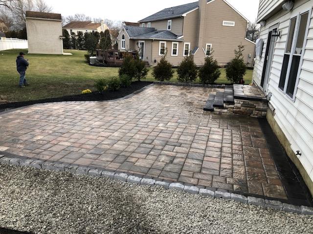 Paver patio with steps next to a house, person standing in the yard.