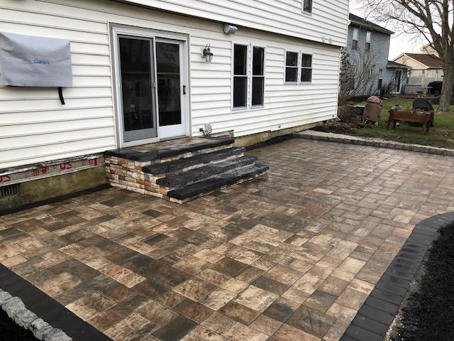 Brick patio with steps leading to a sliding door, next to a white house.
