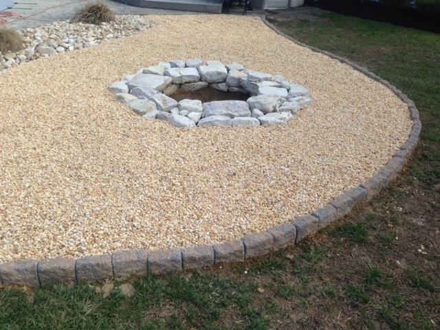 Fire pit in a gravel-covered yard, bordered by stone blocks and grass.