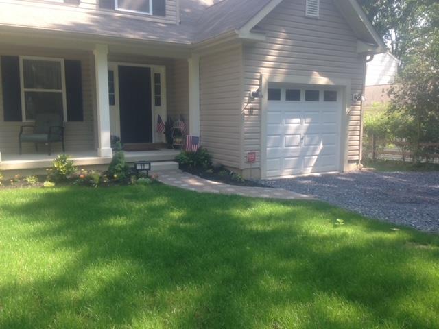 Beige house with a porch and attached garage, a walkway, and green grass.