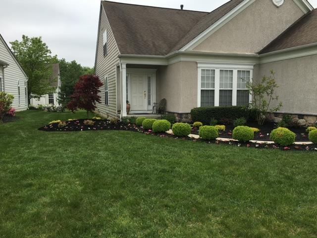A house with a well-manicured lawn and flower beds, set under a cloudy sky.