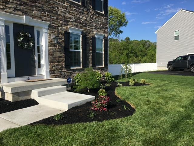House exterior with stone facade, concrete steps, black mulch, and green lawn.