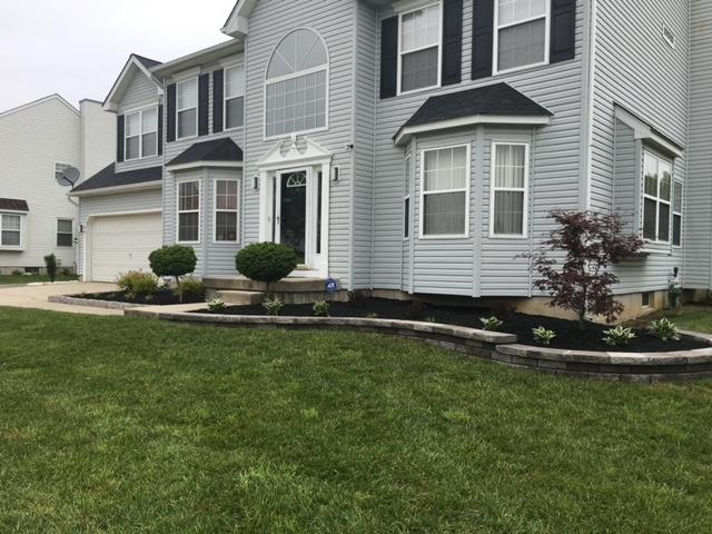Two-story light blue house with black shutters, landscaping with mulch, lawn.