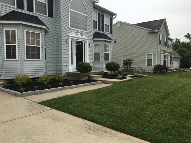 Two-story house with blue siding, a manicured lawn, and flowerbeds with dark mulch and stone borders.
