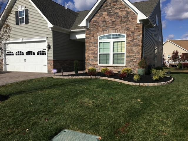 House exterior with green lawn, stone facade, and landscaped flower bed.