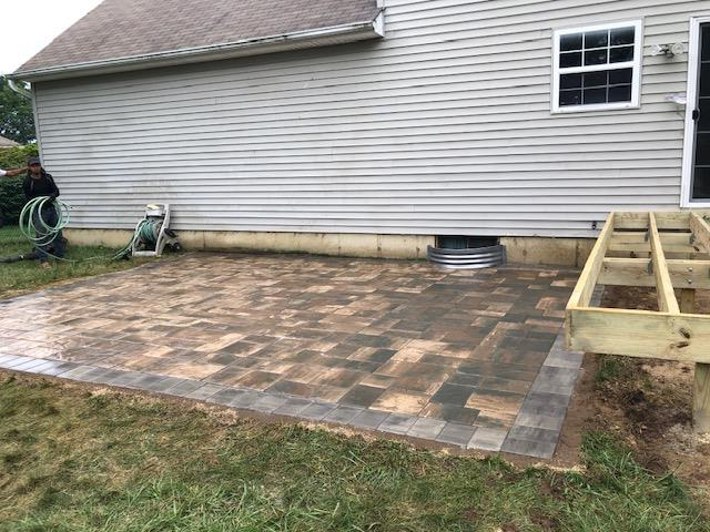 Patio with pavers and wooden deck frame next to a house with gray siding.