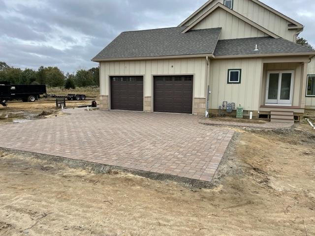 Brick patio in front of a house with two garage doors and a set of glass doors.