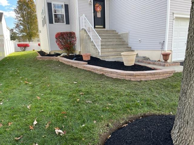 Front yard with a brick-lined flower bed filled with black mulch, steps leading to a door, and a tree.