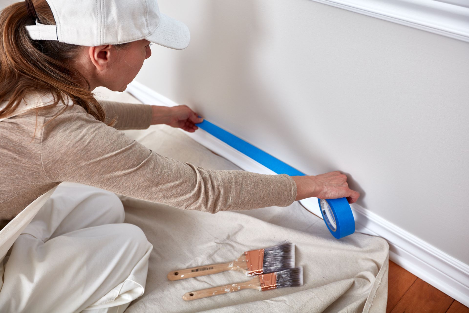 A lady painter who is masking skirting board.