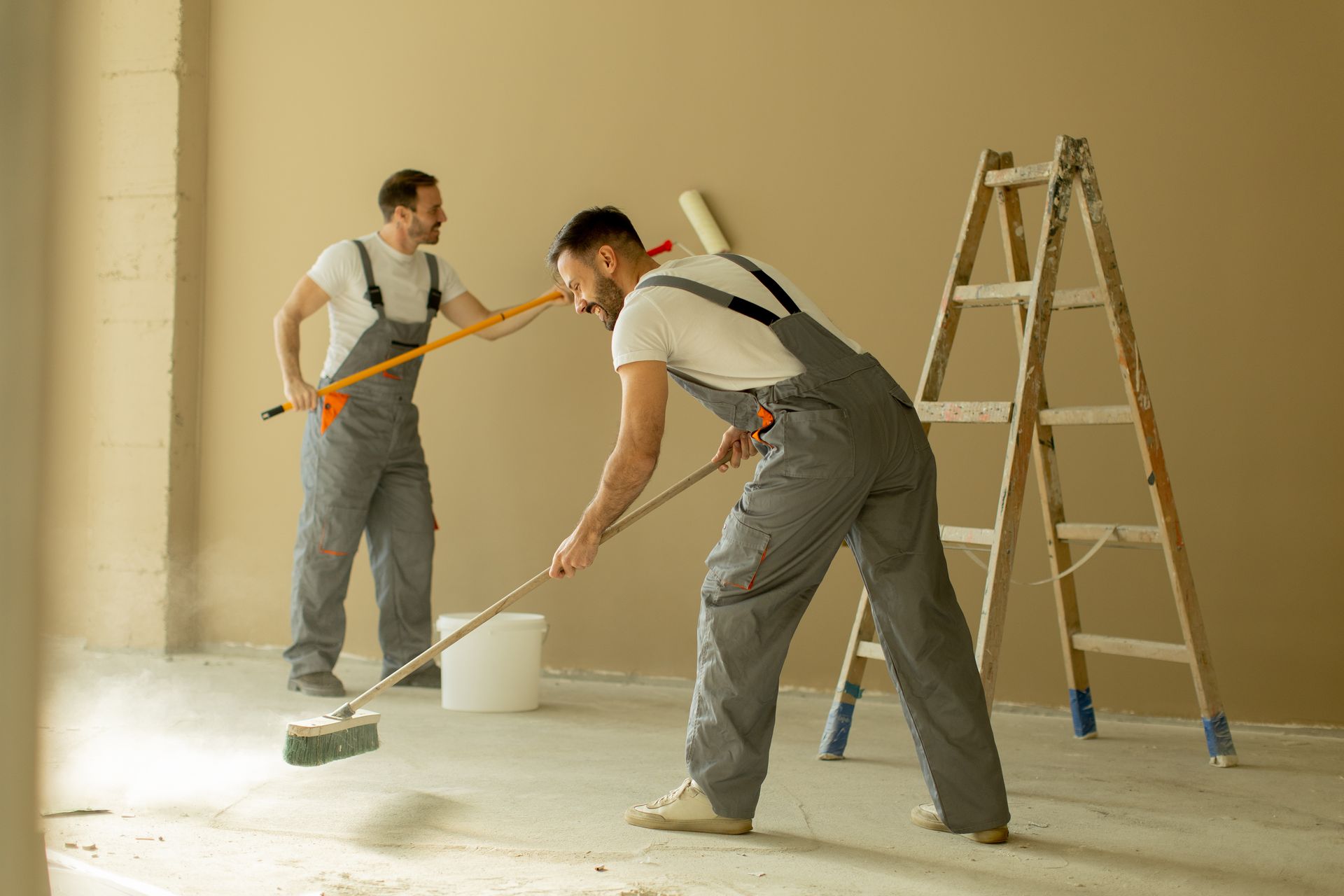 Two men painting an interior wall with a ladder besides them.