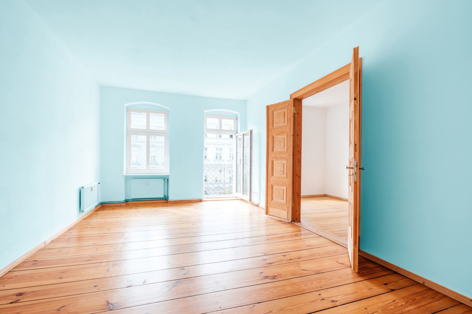 An empty room with light blue-coloured walls and wooden flooring and an open door.