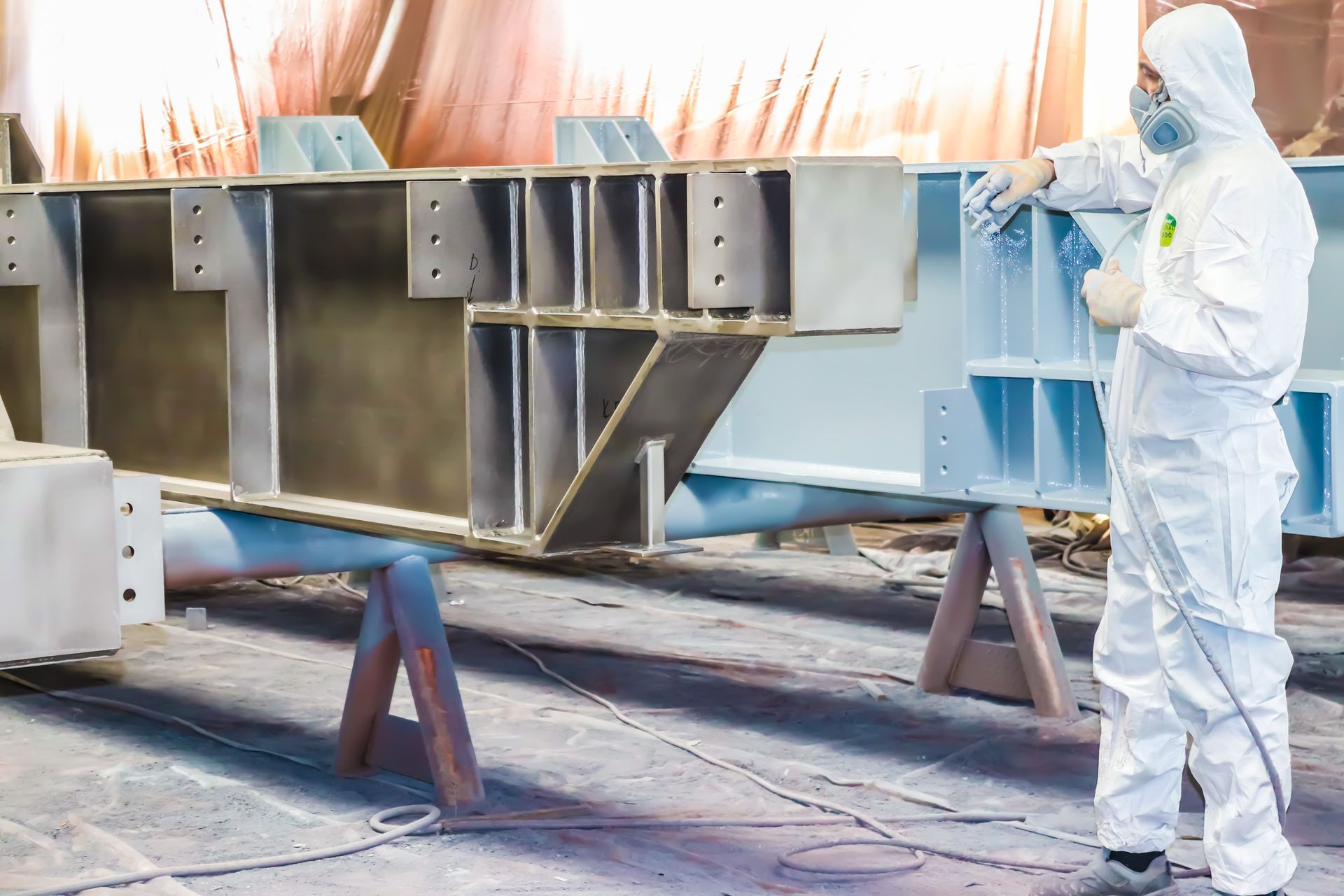 A painter is working to paint a steel structure with a spray gun at an industrial factory. A painter is working to paint a steel structure with a spray gun at an industrial factory.