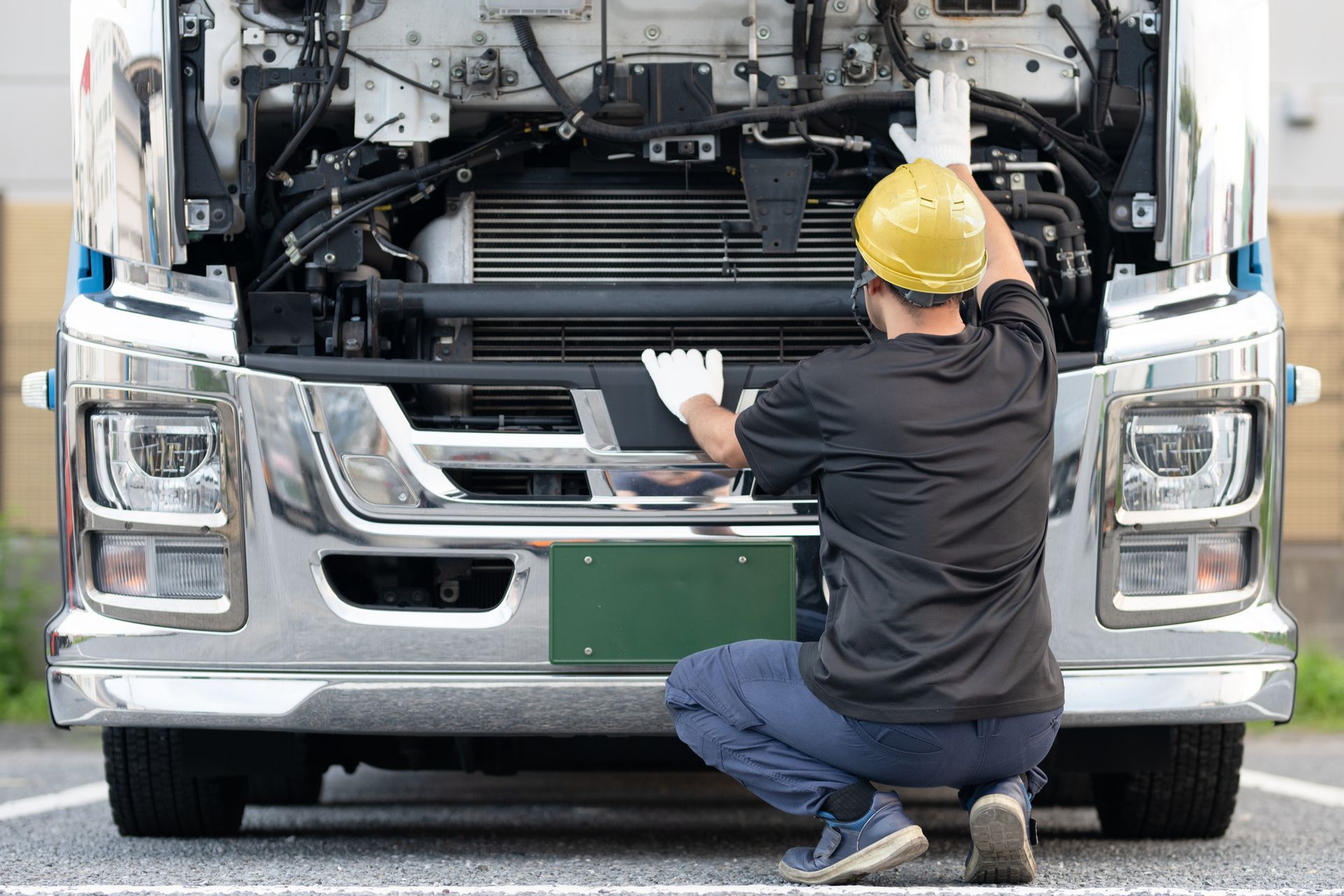 Mechanic in yellow hard hat, inspecting the open hood of a truck.
