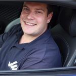 Man in blauw shirt lachend in auto.