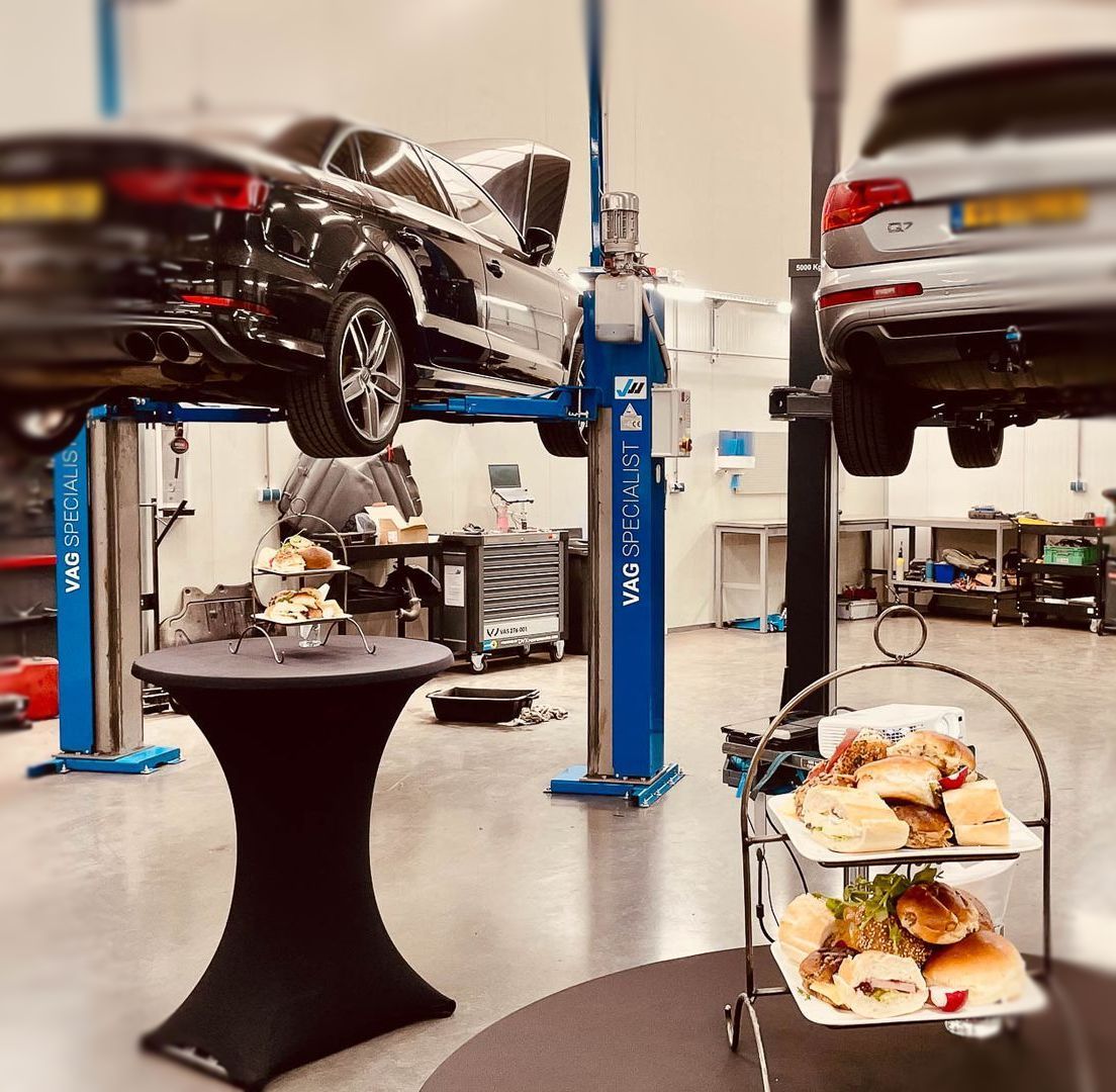 Auto's op liften in een garage met versnaperingen op tafels; catering-evenement.