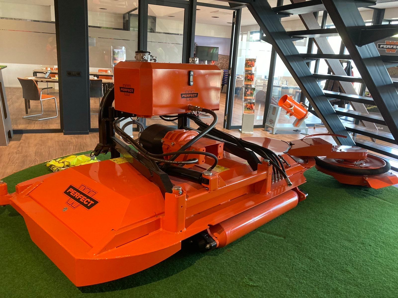 Een grote oranje machine staat bovenop een weelderig groen veld.
