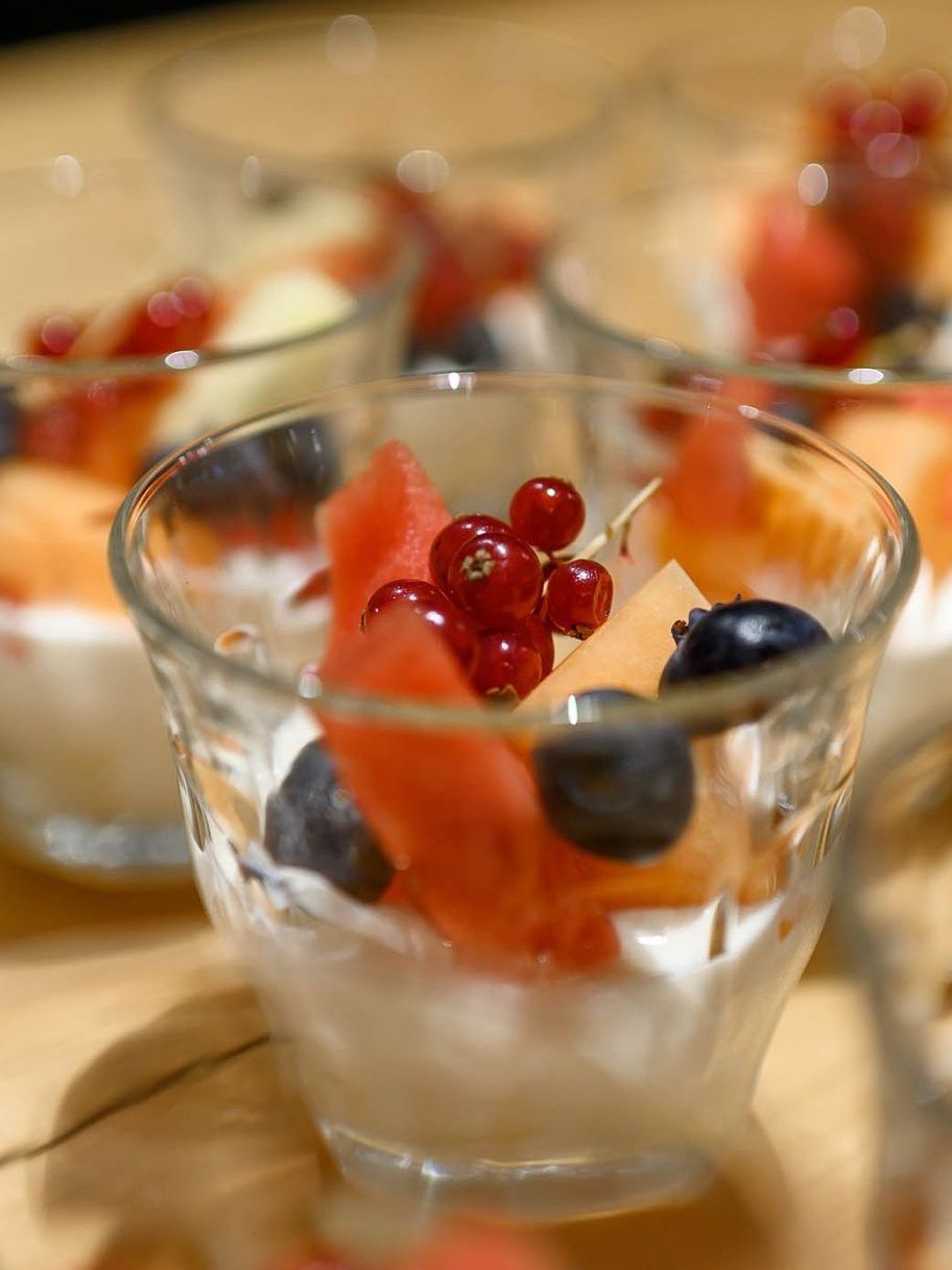 Kleine glazen schaaltjes gevuld met yoghurt en gegarneerd met watermeloen, meloen, bosbessen en rode bessen.