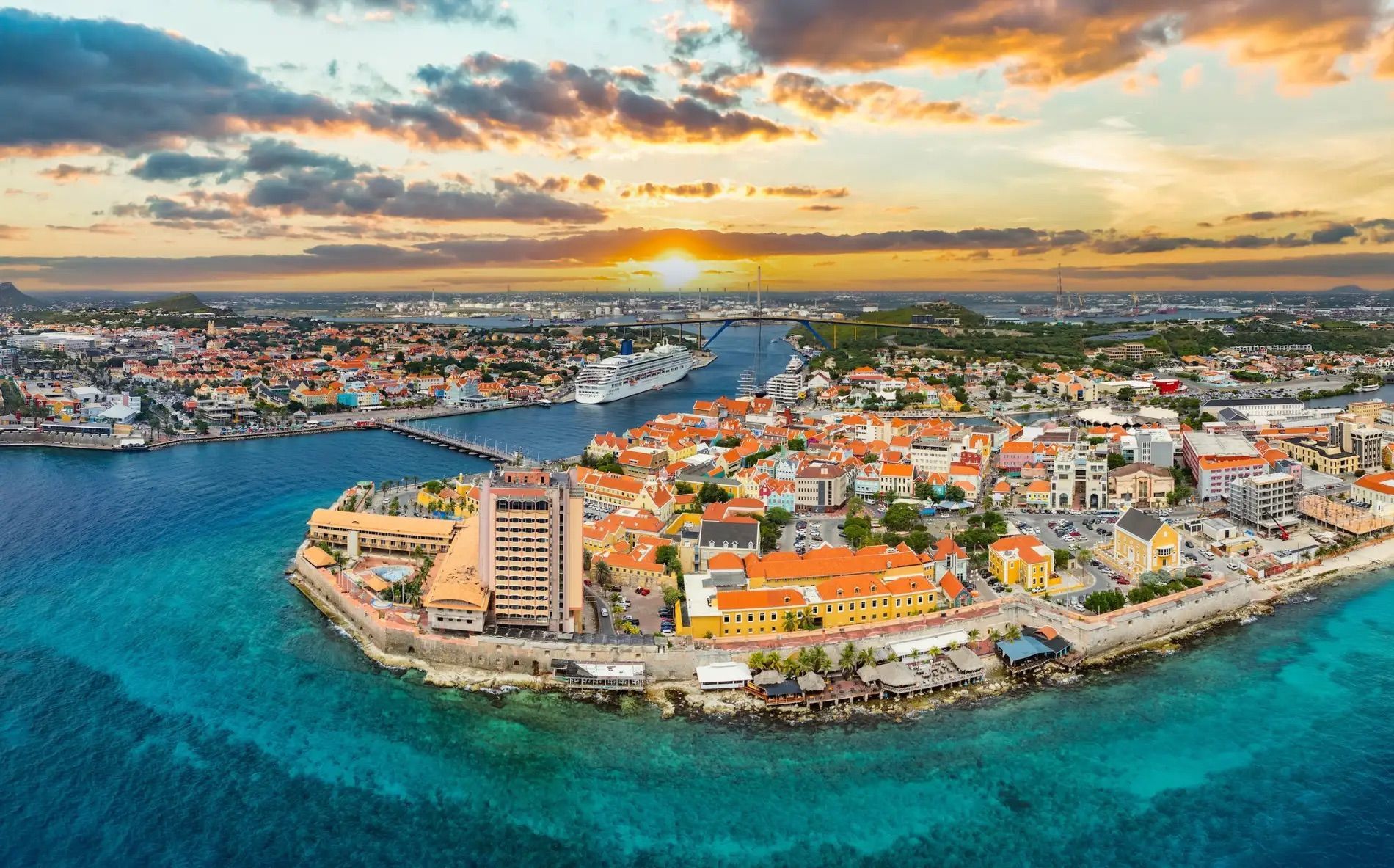 Aerial view of a colorful coastal city on a peninsula, surrounded by turquoise water at sunset