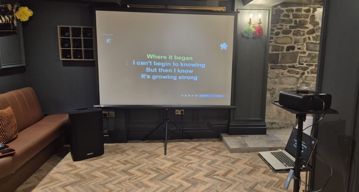 Conference room with projector screen showing a presentation, stone wall, speakers, and a tripod-mounted camera.