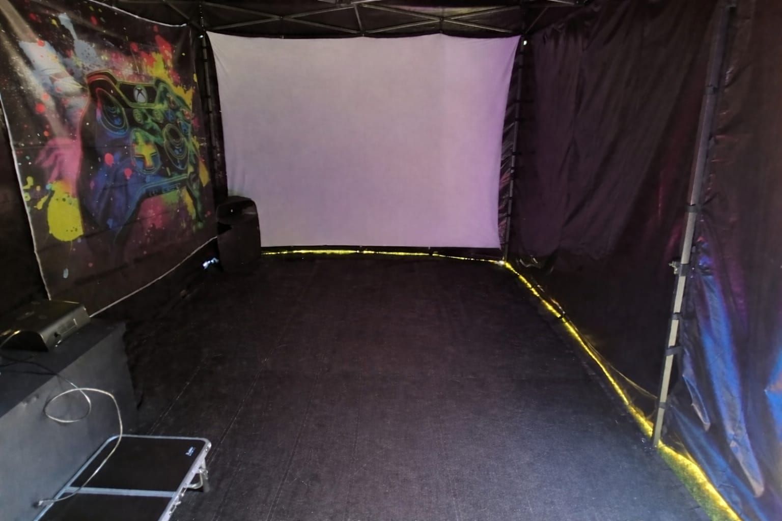Empty indoor tent with black floor, white screen at back, and colorful wall art on the left