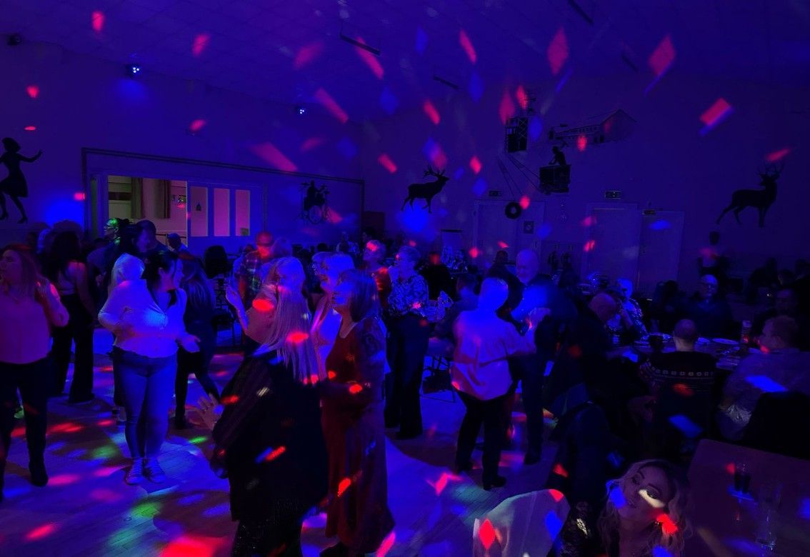 Crowded indoor dance party with purple and red laser lights and people dancing