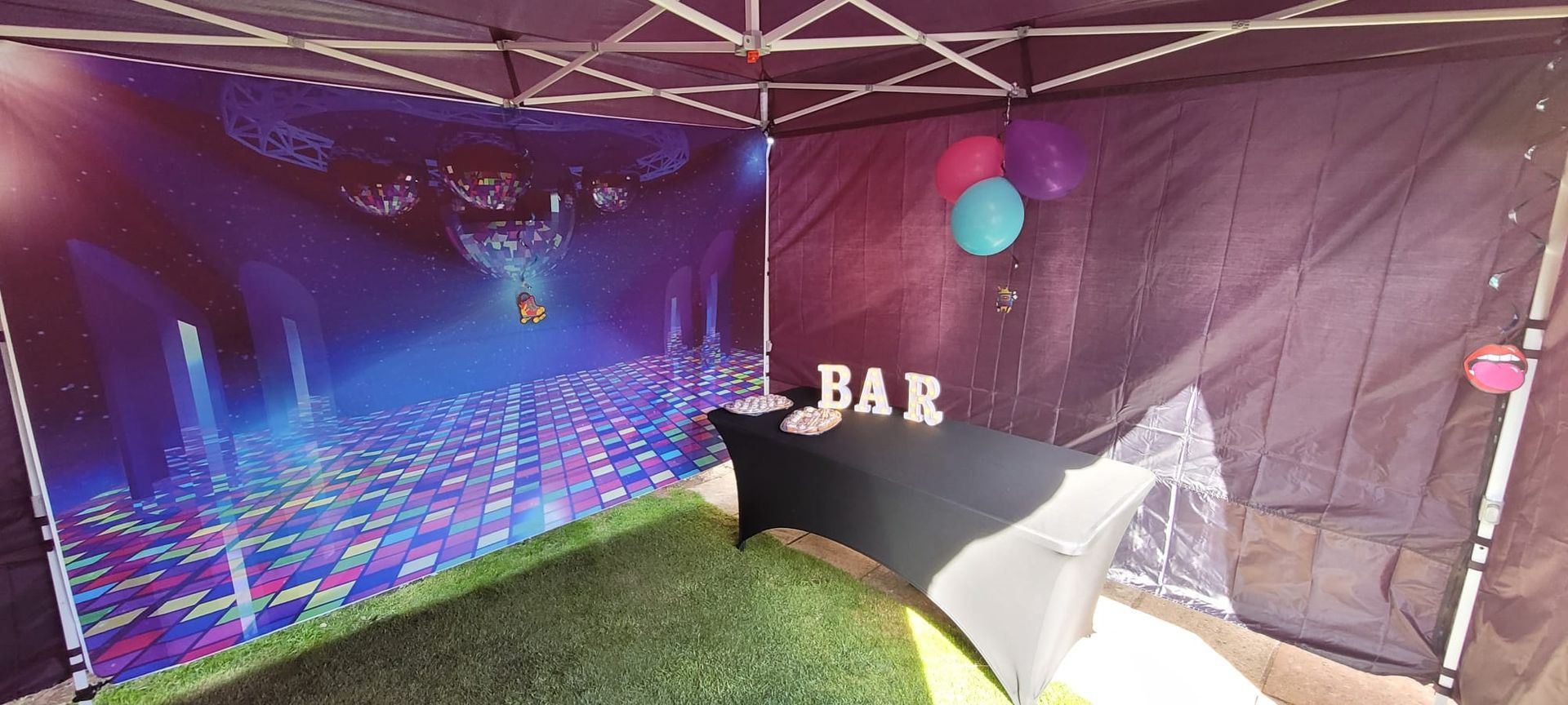 Purple-lit party tent with a BAR sign, disco floor lights, and a white-covered table on grass