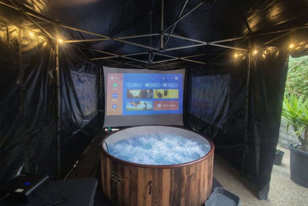 Outdoor black tent with a round wooden hot tub and a small screen at the back