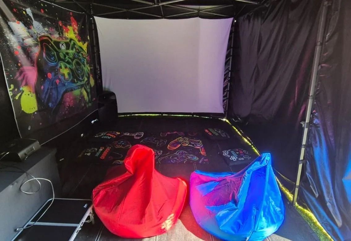 Small black tent room with a white screen, colorful wall art, and red and blue bean bags.