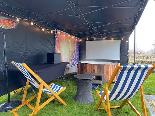 Outdoor movie setup with two striped chairs, round table, projector screen, and bar under a canopy