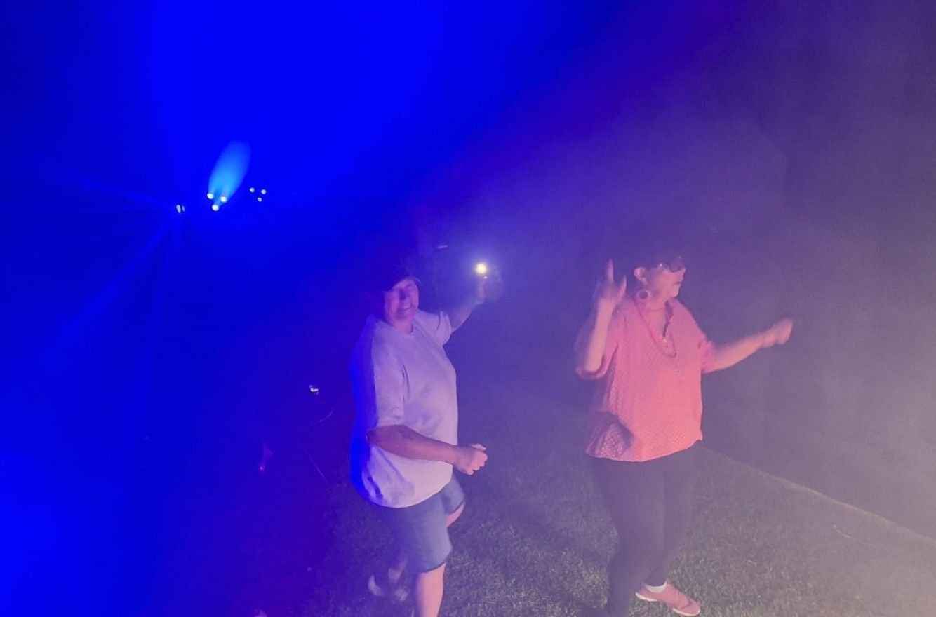 Two people walking through colorful fog at a nighttime event, lit by blue and orange lights.
