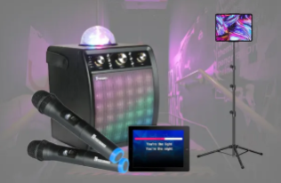Karaoke setup with two microphones, a glowing speaker, tablet display, and TV on a stand