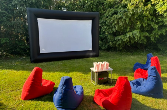 Outdoor movie setup with bean bags facing an inflatable screen on a grassy lawn