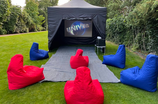 Outdoor black canopy tent with screen, red and blue beanbags on grass, arranged like a small lounge