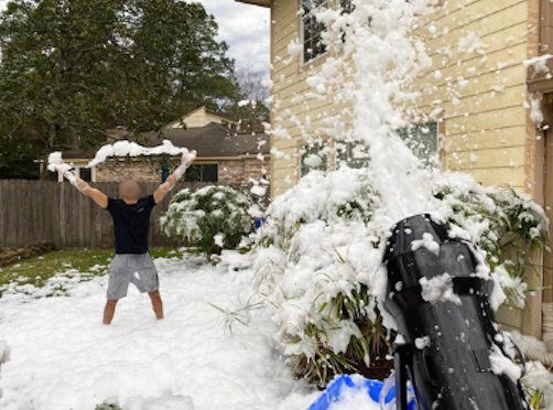 Person holding up a snow-covered object in a snowy yard beside a house