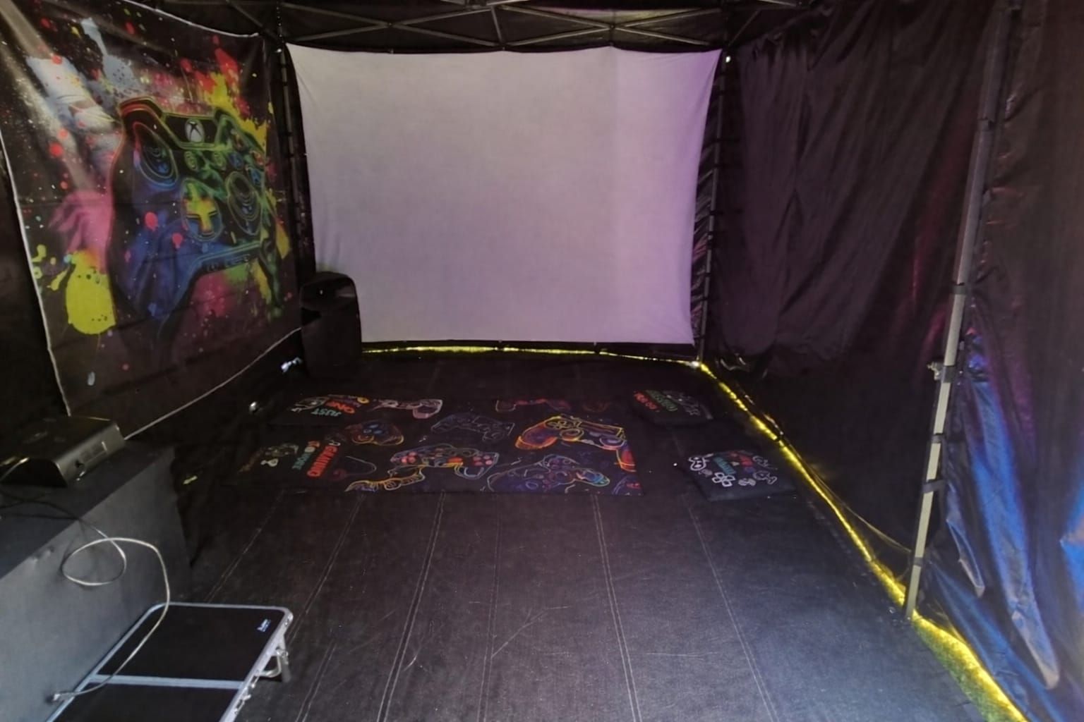 Empty dark room with black walls, colorful graffiti panels, and a white projection screen at the back.