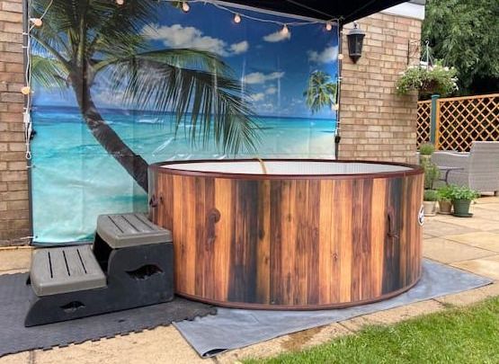 Wooden hot tub under a canopy with tropical beach backdrop and benches in a backyard patio
