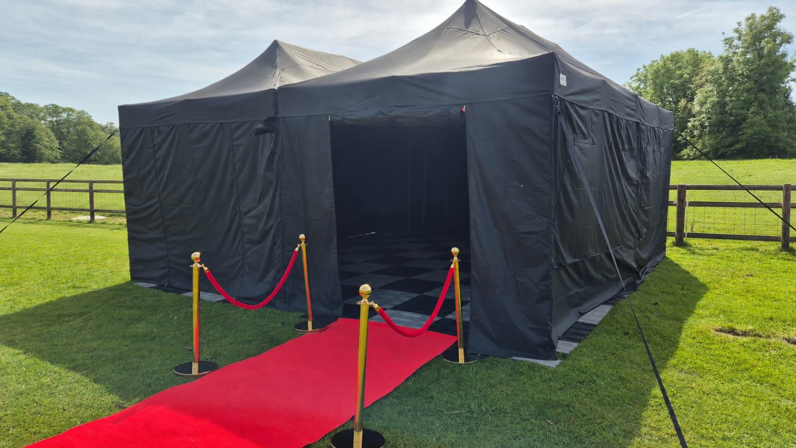 Black marquee tent on a lawn with a red carpet entrance and stanchions