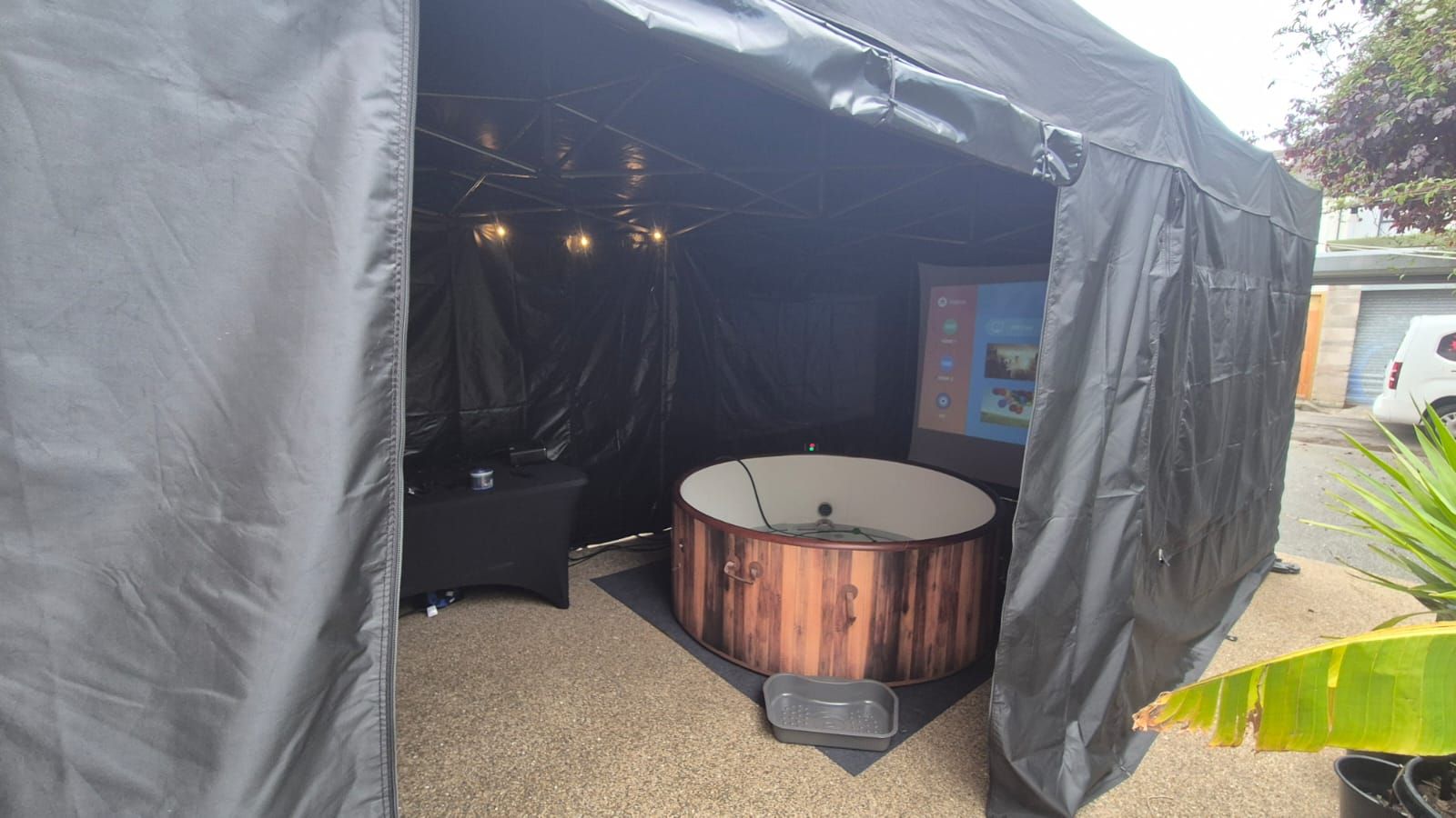 Black tented outdoor hot tub area with a copper-colored wood-fired tub on gravel.
