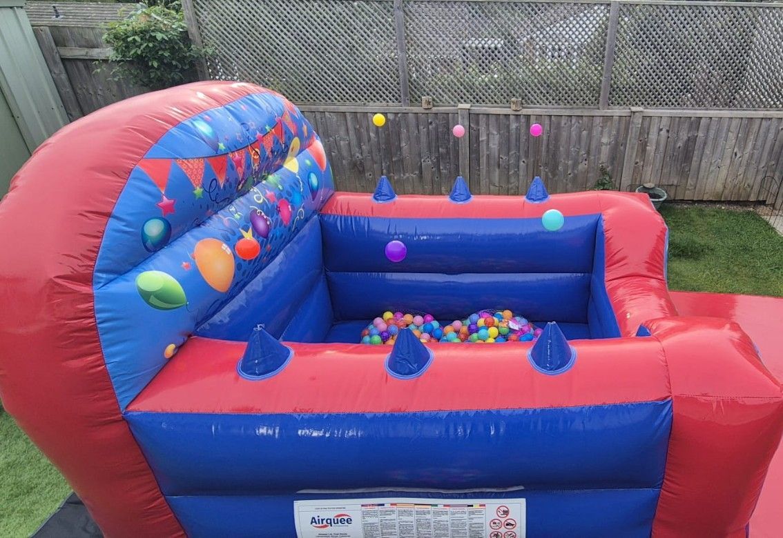 Red and blue inflatable bounce house with ball pit and colorful balls in a fenced backyard