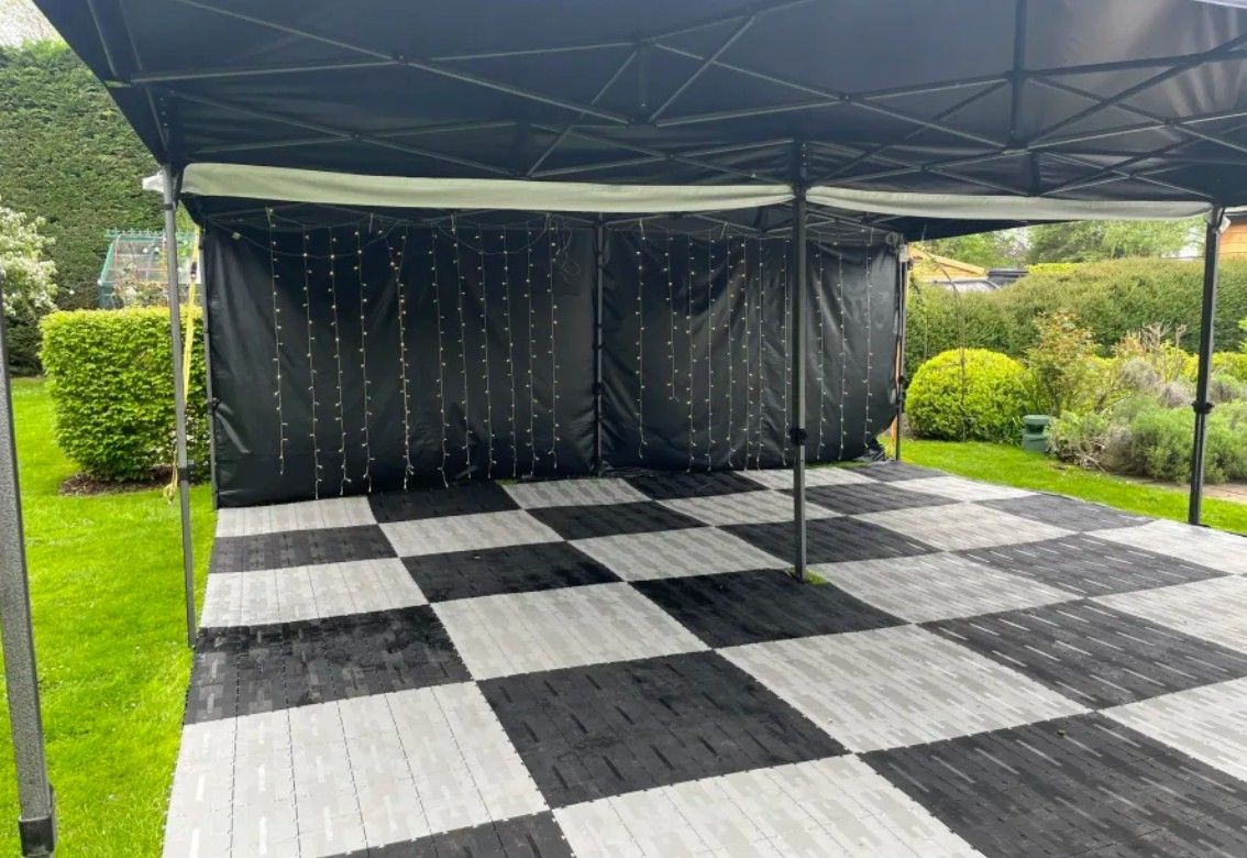 Empty outdoor canopy with black drapes and black-and-white checkered flooring on a green lawn