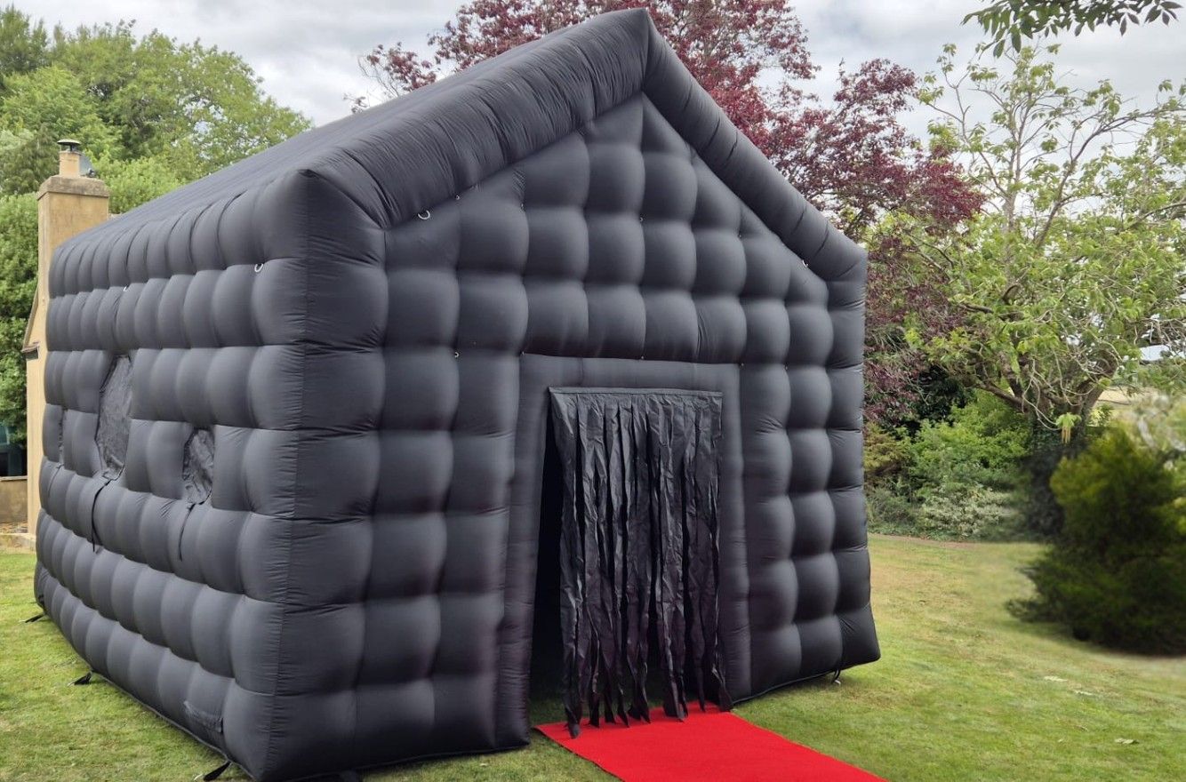 Black inflatable haunted house with a red carpet entrance in a garden