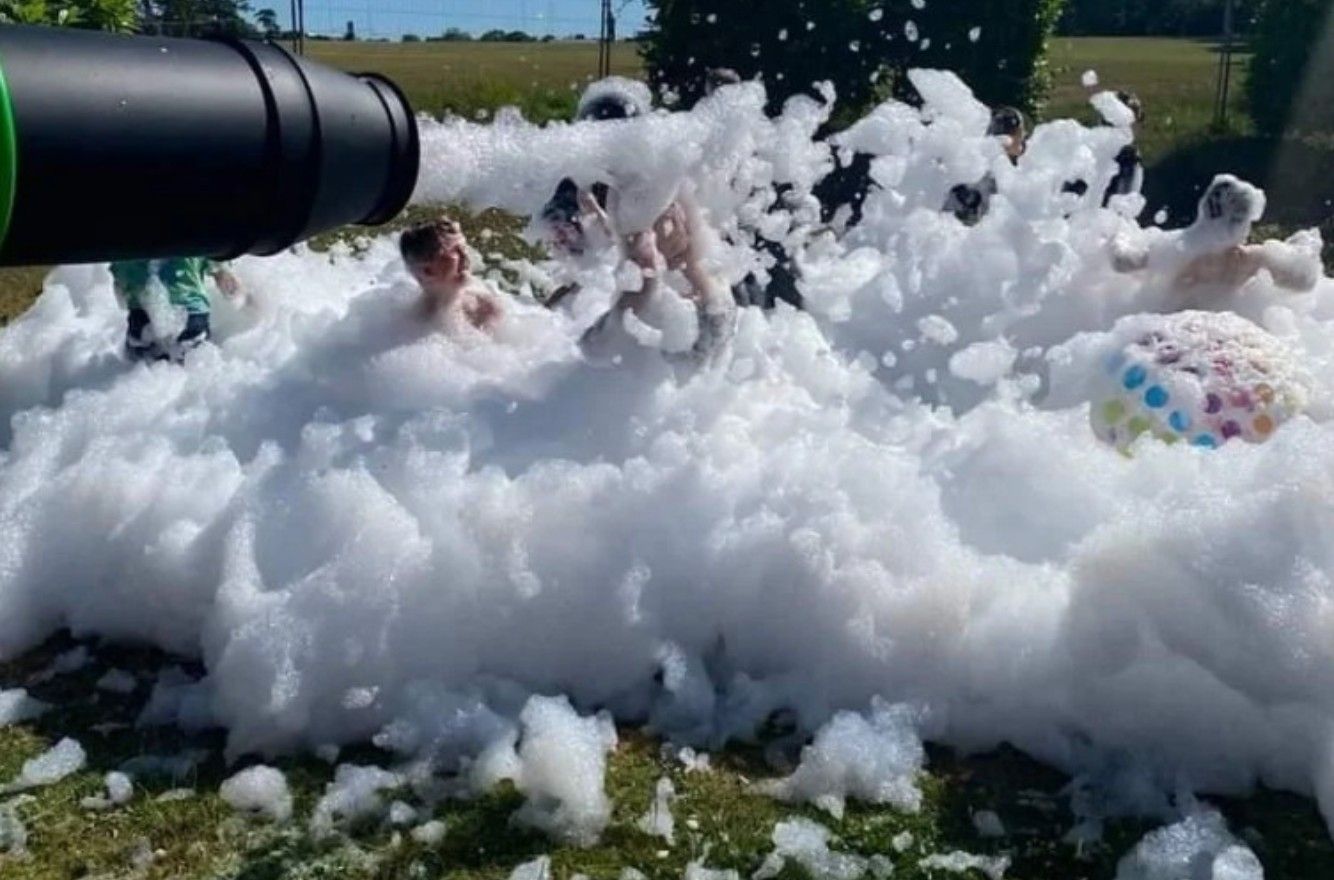 Children playing in a giant pile of white foam outdoors near a black hose