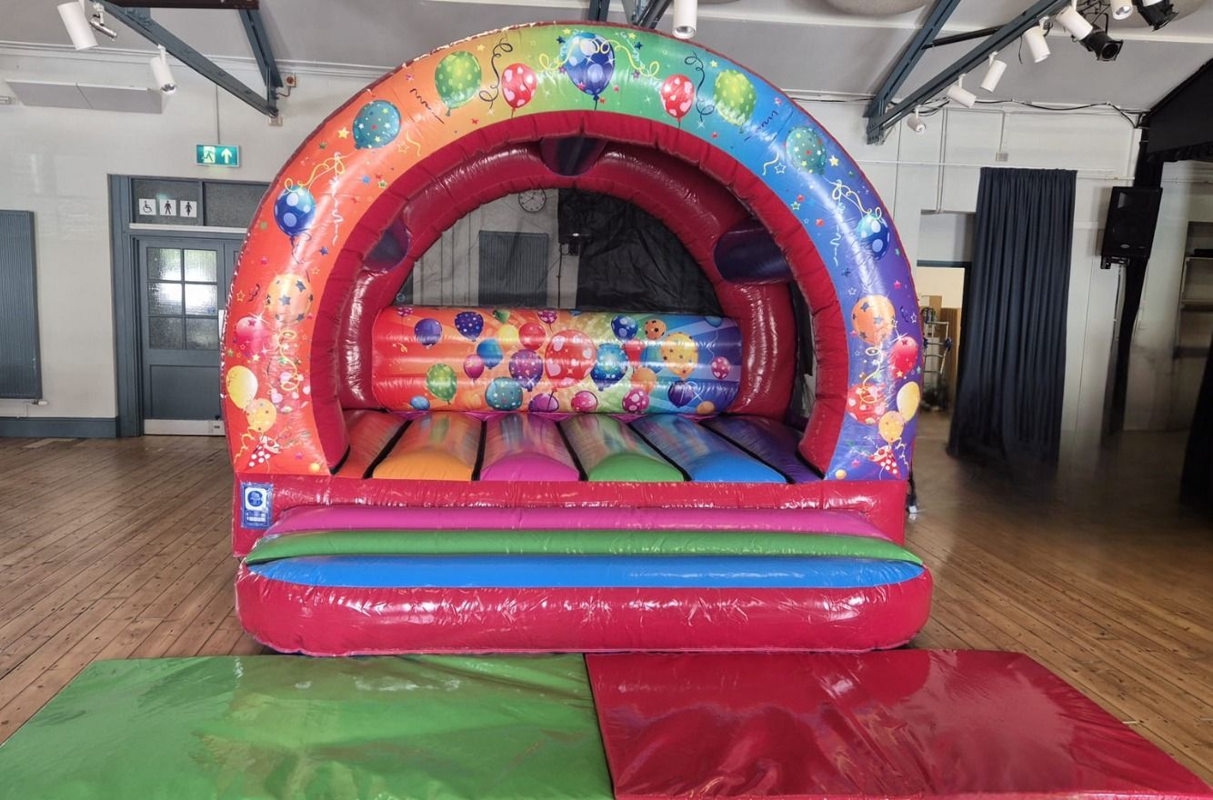 Colorful inflatable bounce house in a gym with red, blue, and green mats in front
