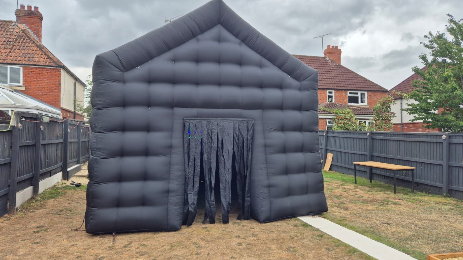 Black inflatable tunnel tent in a backyard, with a central doorway and fenced houses in the background