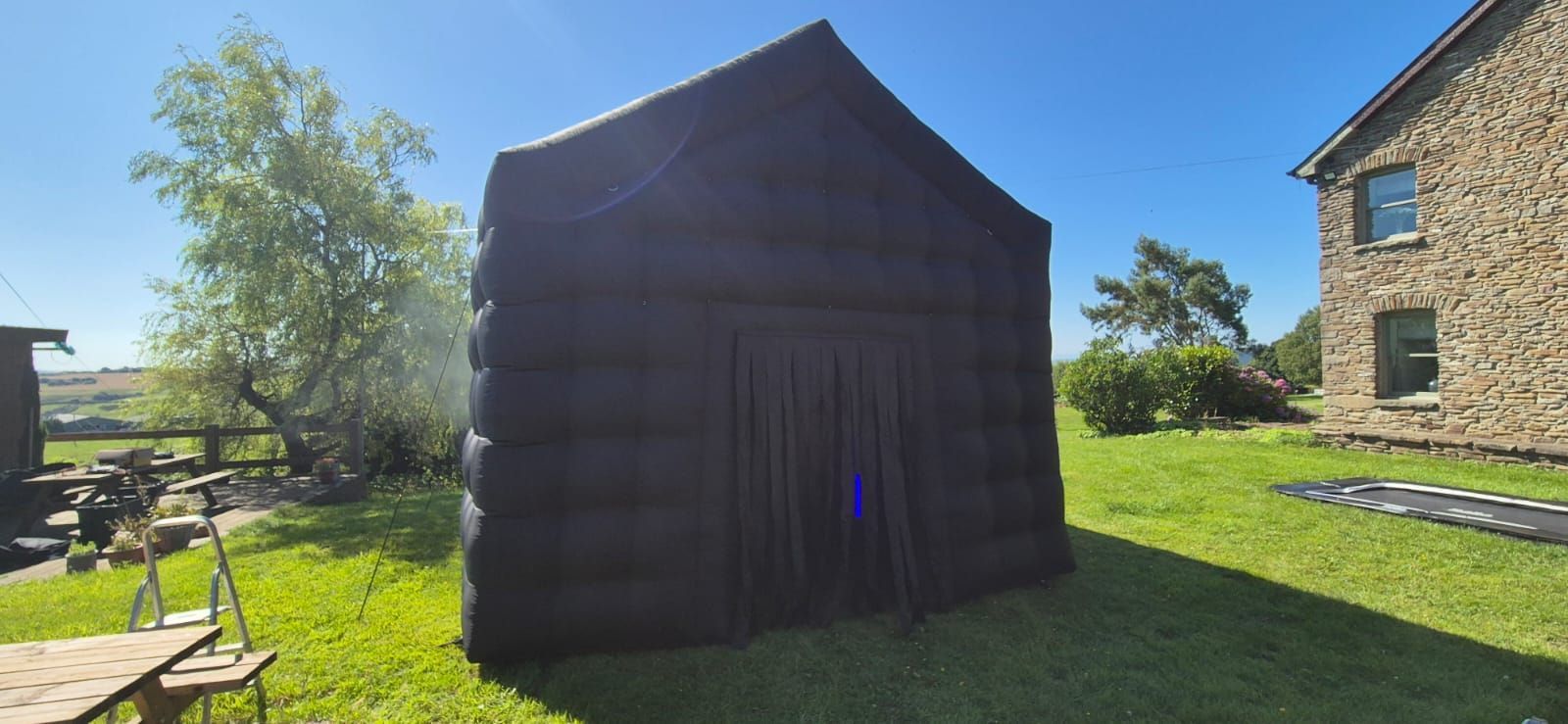 Dark inflatable night club on a grassy lawn beside stone buildings under a blue sky
