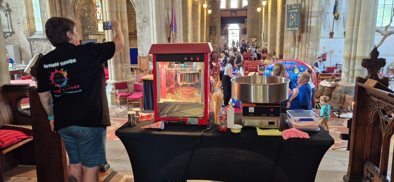 Person at a table with a red framed display and a silver machine in a church-like interior with a crowd beyond
