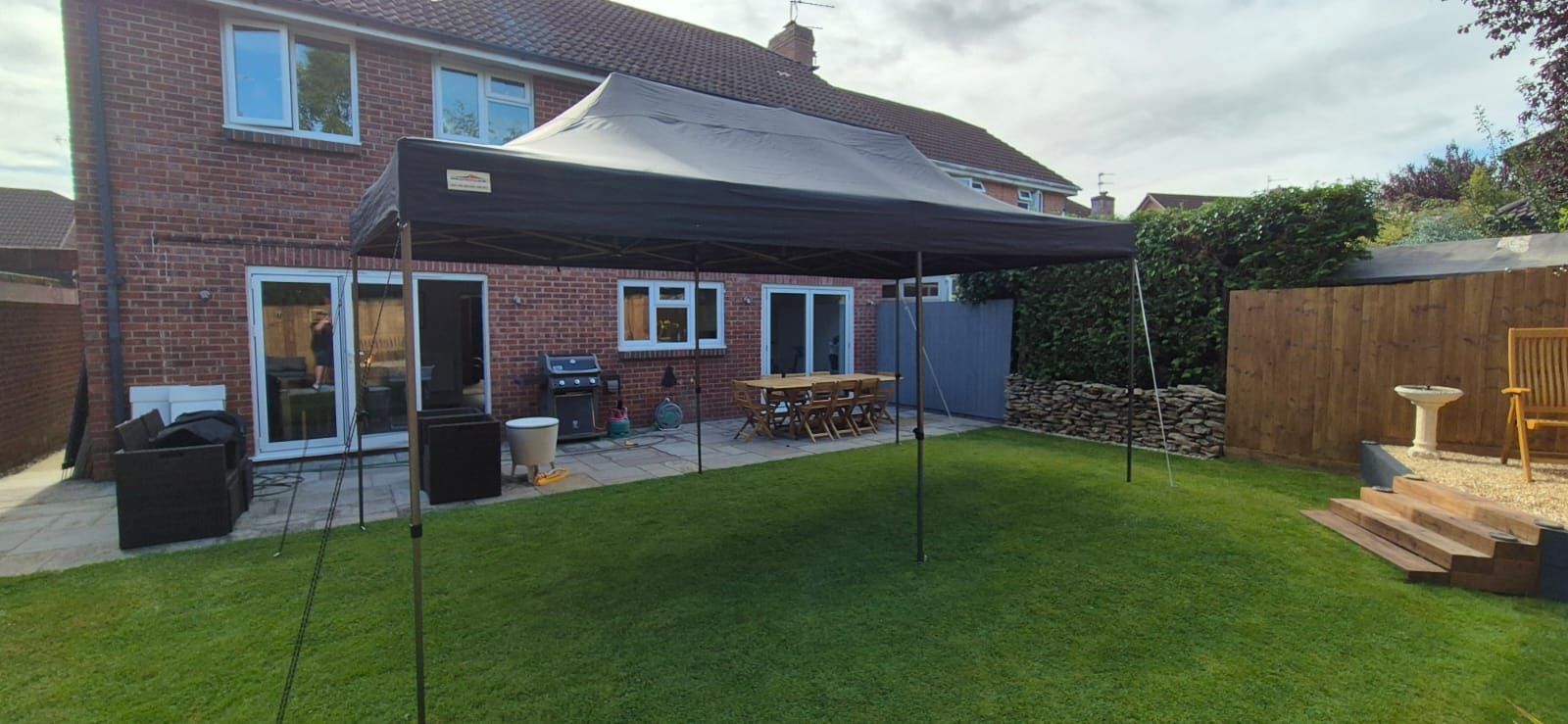Backyard with a brick house, lawn, patio furniture, and a small wooden deck under a cloudy sky