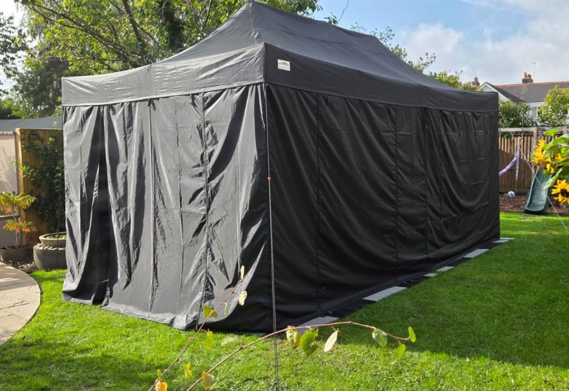 Black pop-up canopy tent set up on a grassy backyard lawn in sunny weather